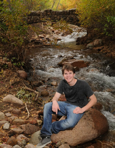 senior sitting on rock near creek